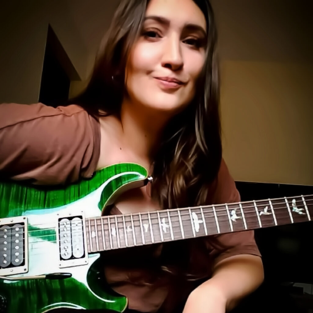 Bailey Eghott smiles softly holding a green bass guitar.